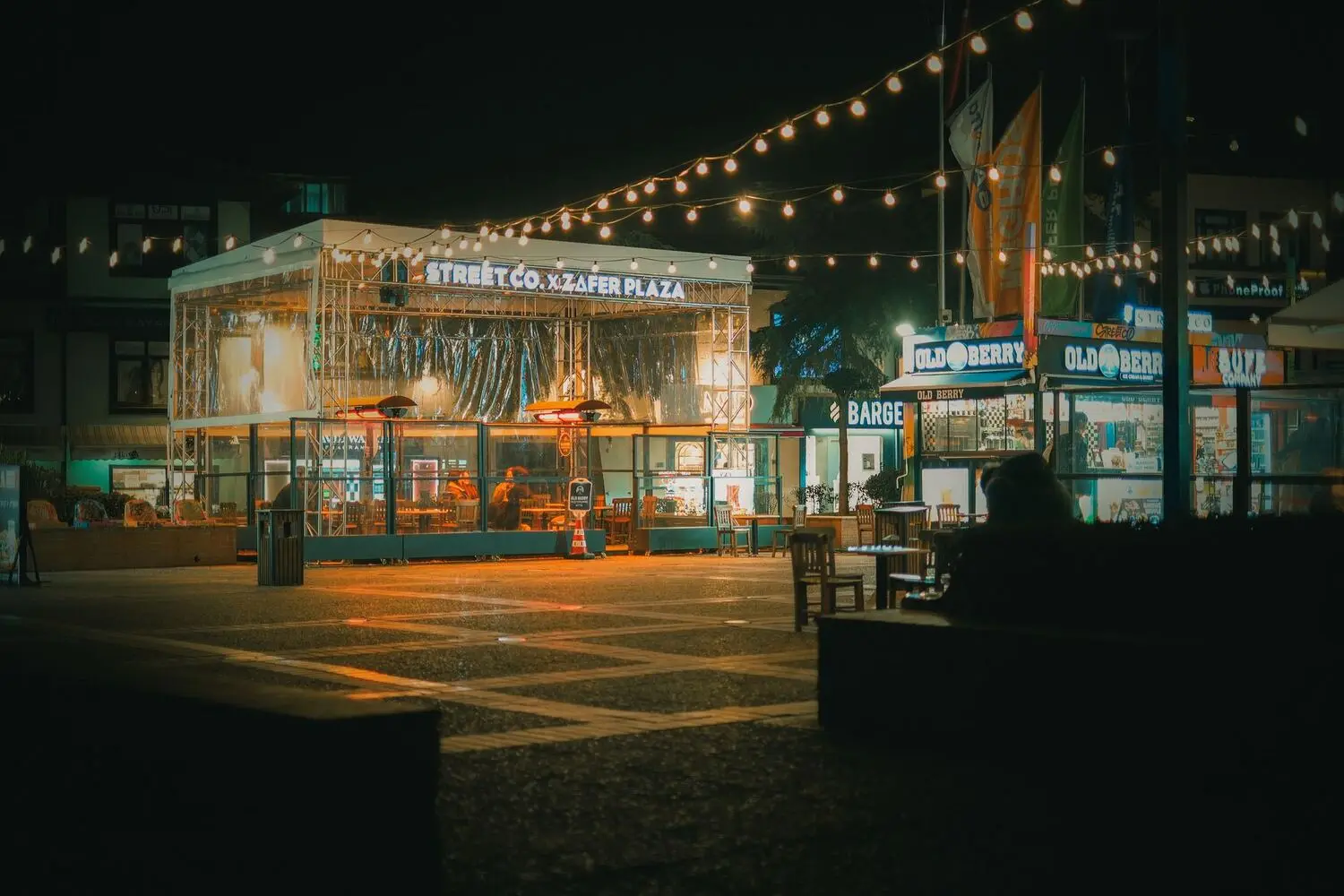 Lit shopfronts and a plaza at night